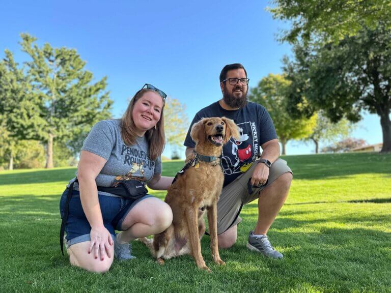 A man and a woman pose for a portrait with their dog in a park