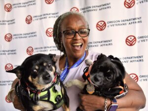 A smiling veteran holds two dogs.