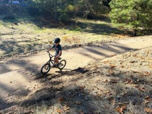 A child rides a bike on a dirt trail.