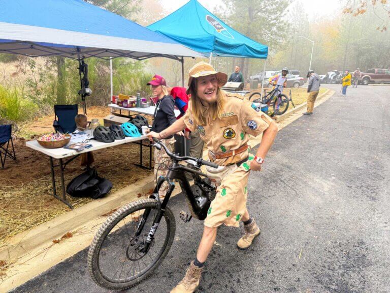 A mountain biker walks his bike across a parking lot.
