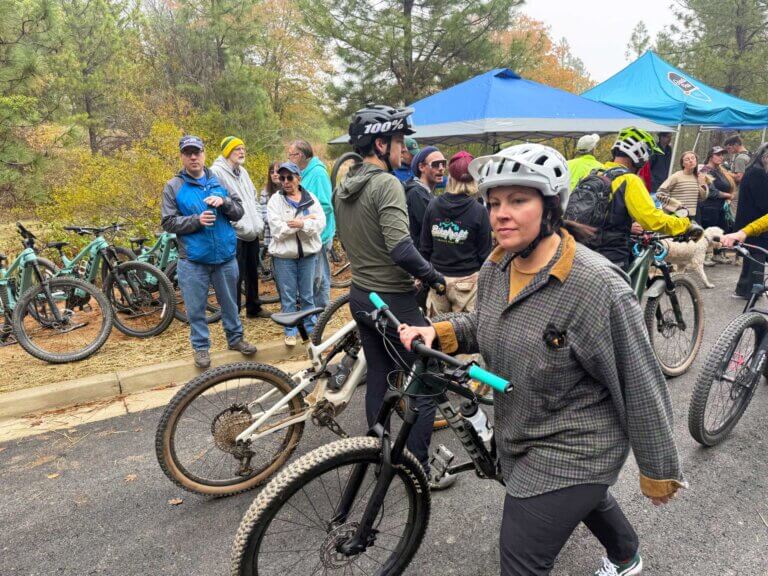 A mountain biker walks her bike across a parking lot.