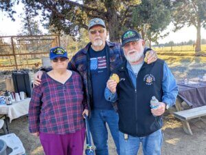 Three older veterans pose for the camera during an outdoor meal.